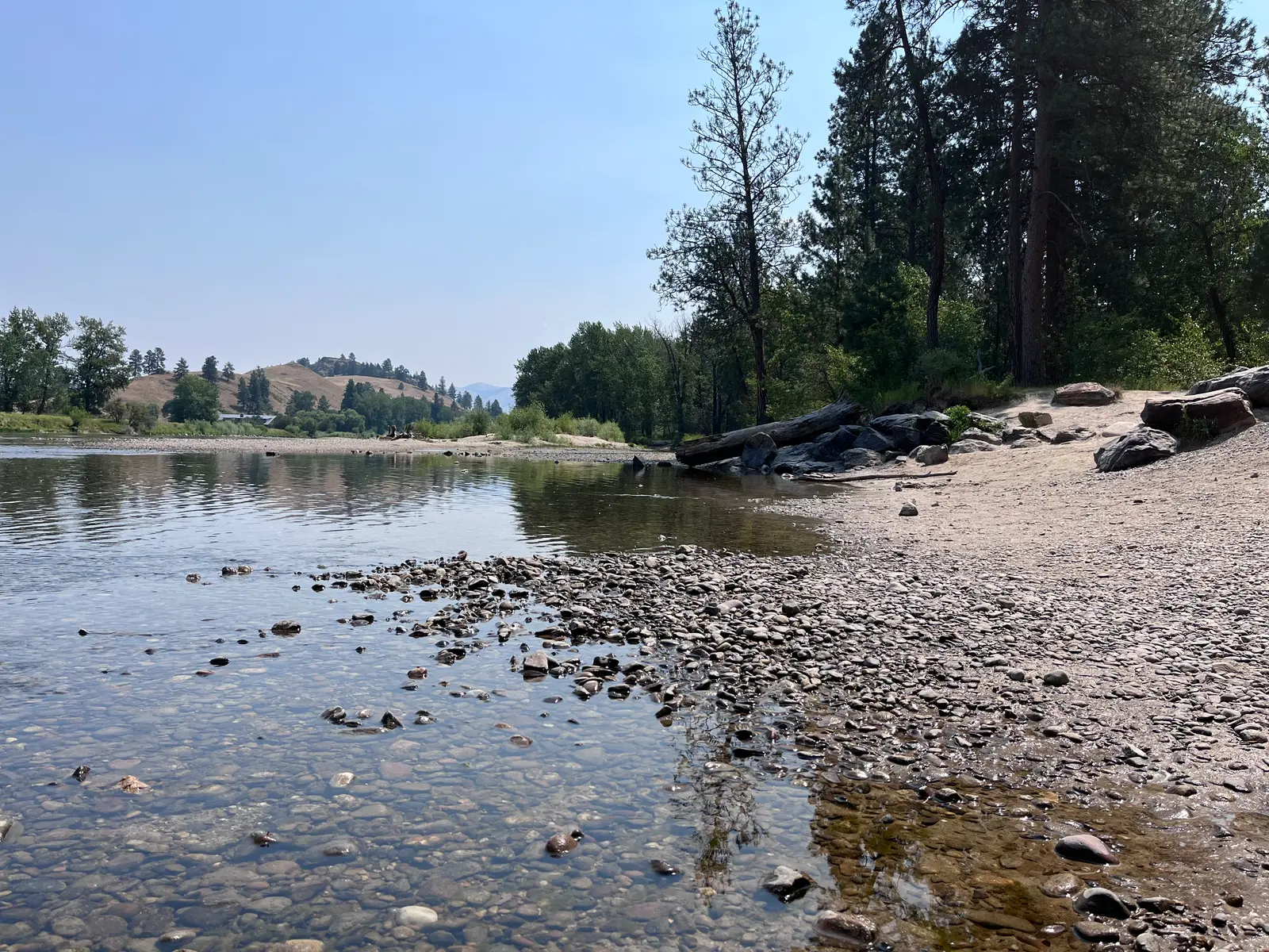 A view of a river with a rocky shoreline and trees along the bank.