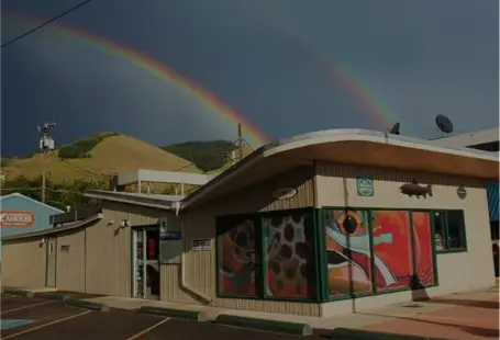 A double rainbow arcs over a building with a mural in a hilly landscape.