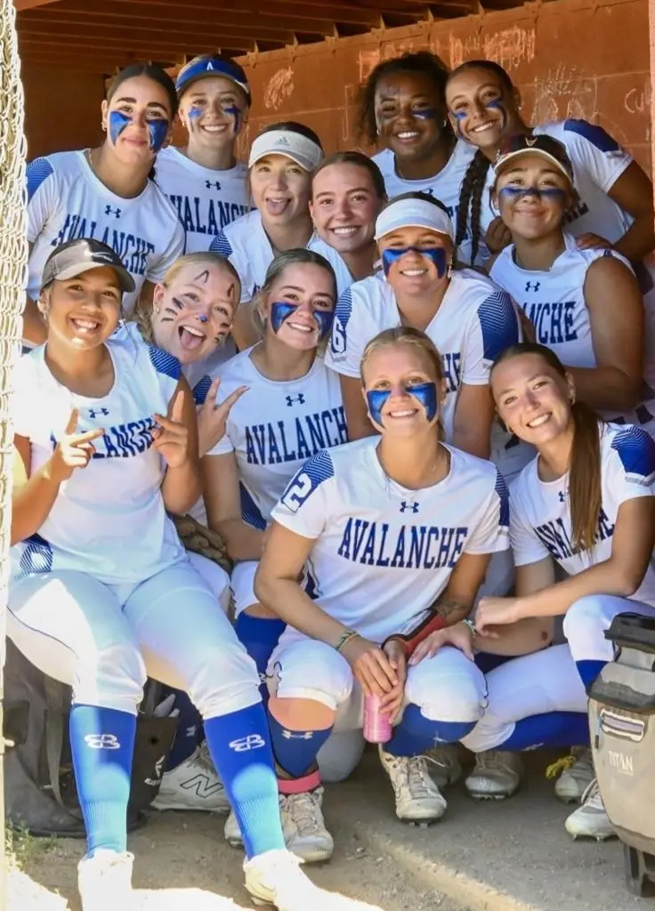 A softball team poses for a group photograph while wearing matching uniforms and eye black.
