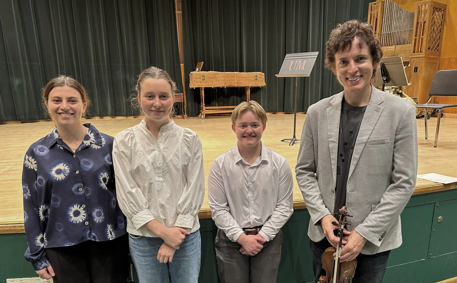 A music instructor and three students stand together on a stage.