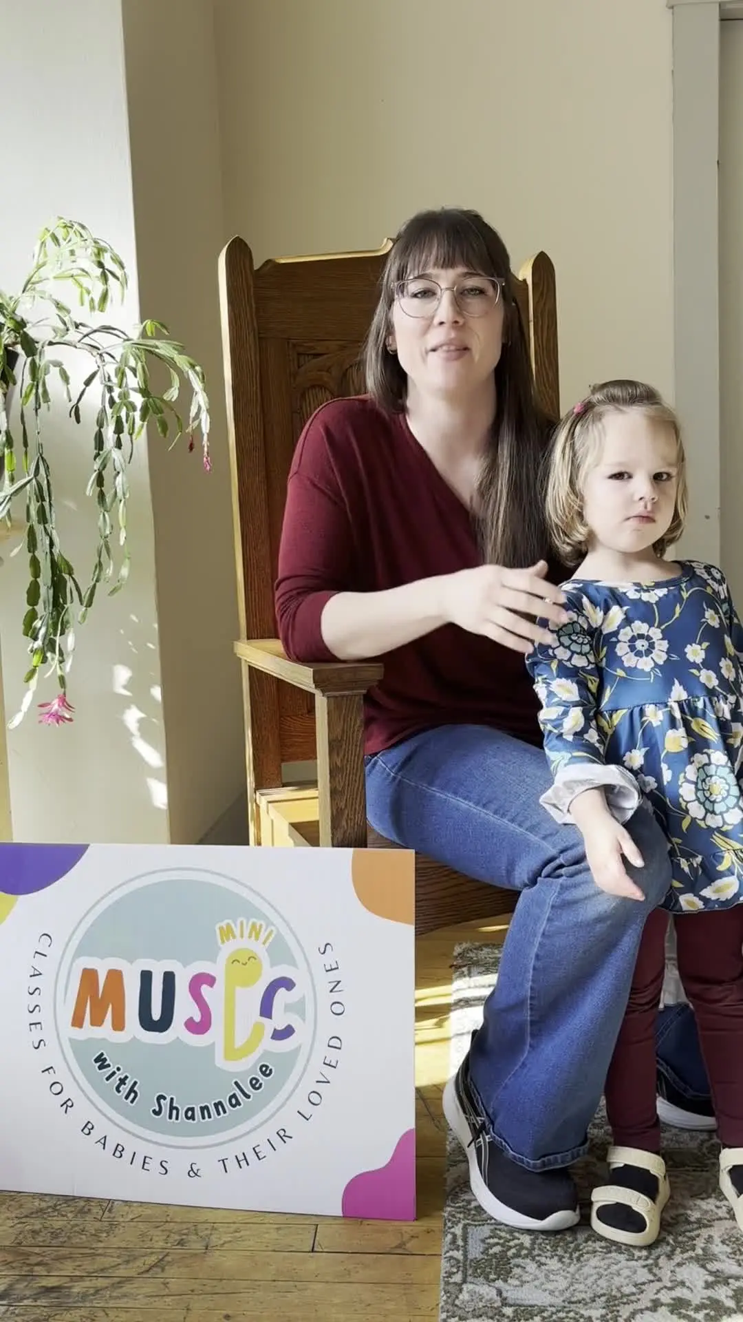 A woman and a young child are posed together next to a sign for music classes.