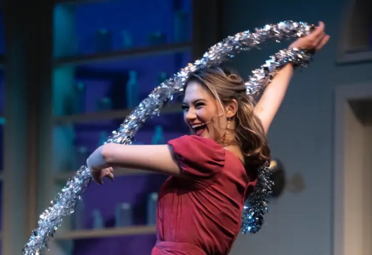 Character in She Loves Me dancing with tree garland (2022)