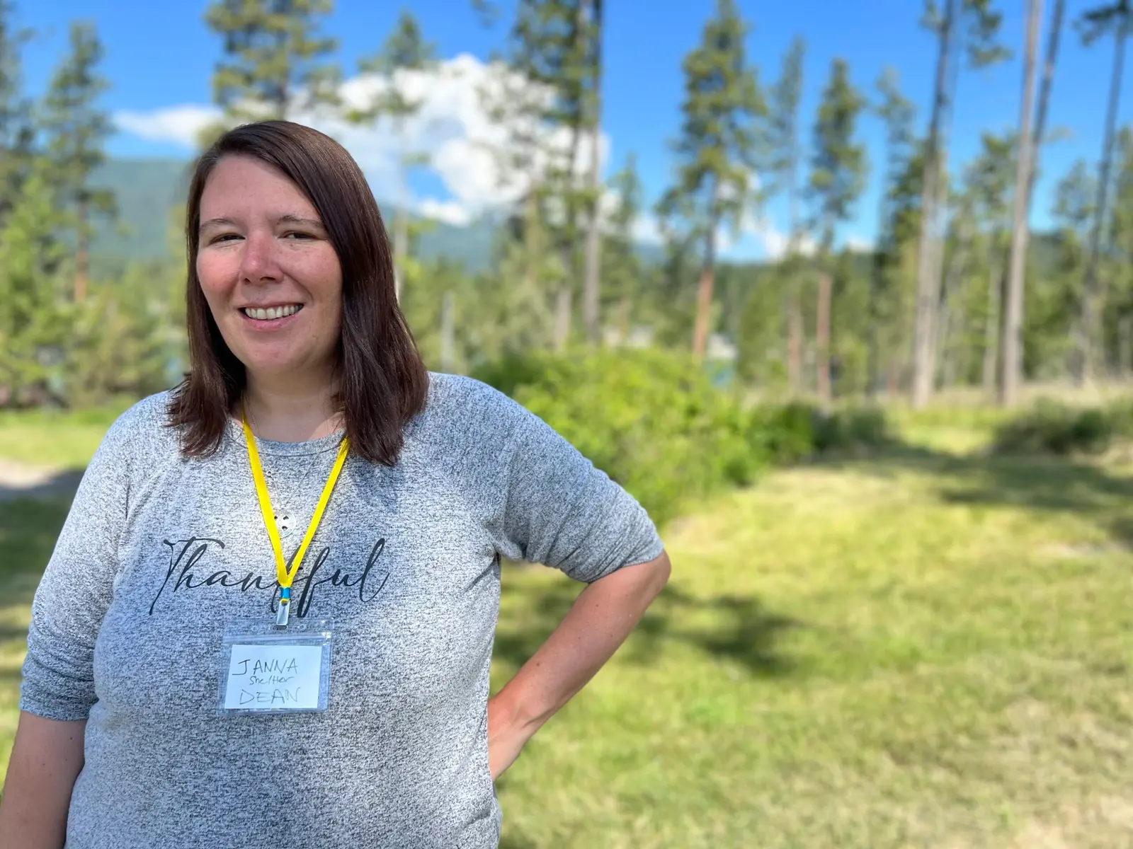 A smiling woman stands outdoors wearing a name badge.
