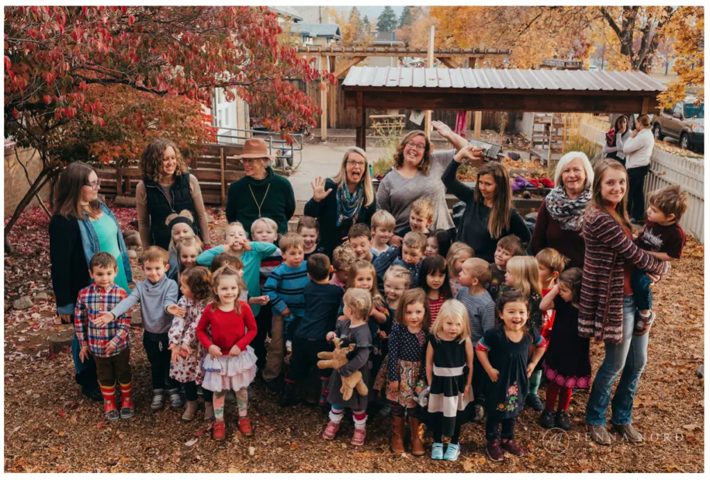 A large group of children and adults posing together in a yard during autumn.