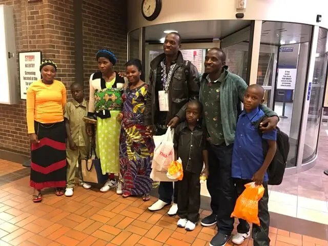 A group of adults and children are standing together in an indoor entryway.