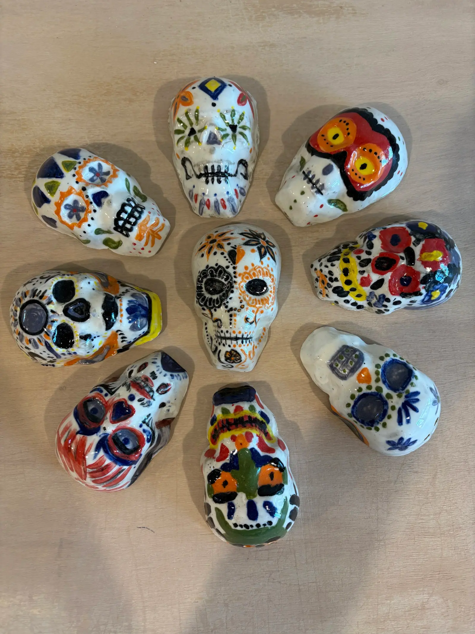 A collection of colorful, hand-painted ceramic sugar skulls arranged on a wooden surface.