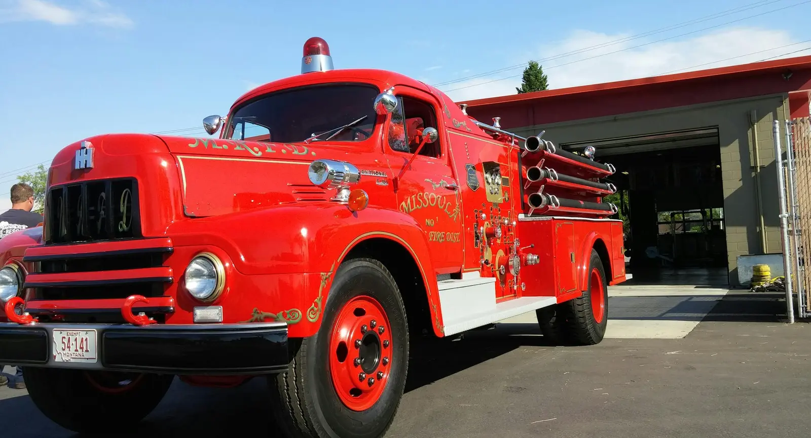 A vintage red fire truck parked in front of a fire station.
