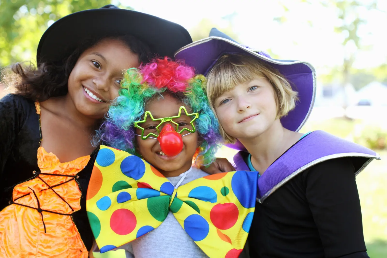 Three children in Halloween costumes pose together and smile at the camera.