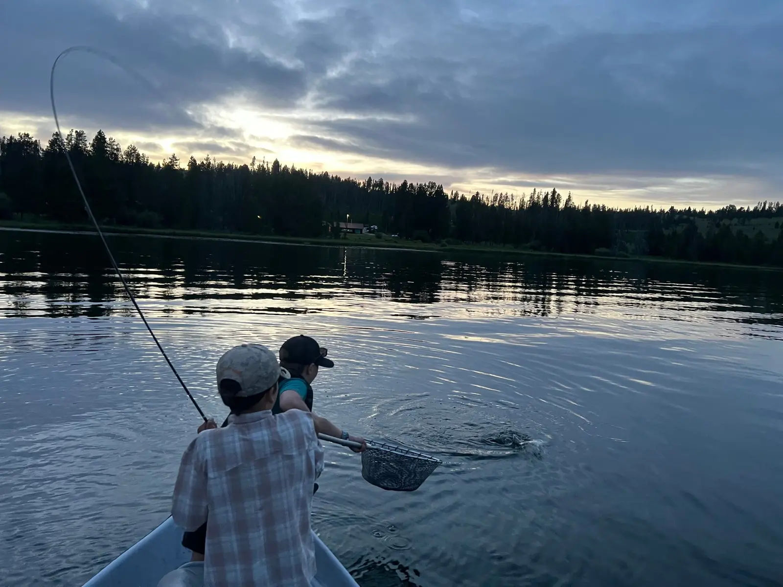 Two children in a boat fish together on a lake at sunset.