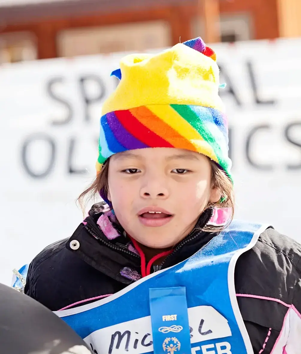 A child wears a rainbow hat and a blue bib while participating in an event.