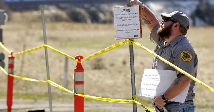 A man in a uniform puts up a caution sign near yellow construction tape.