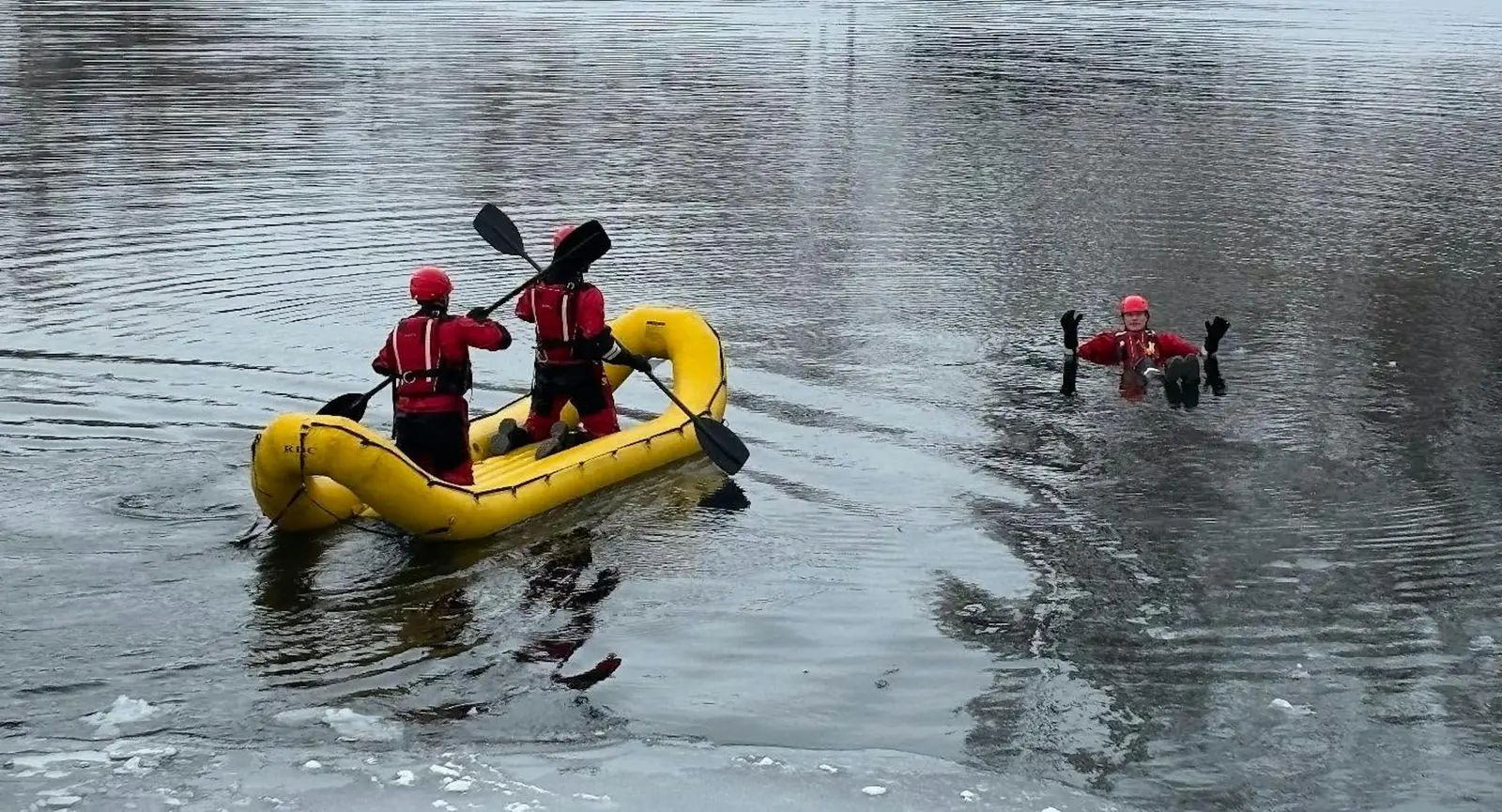 Two people in a yellow rescue boat approach another person in the water during a cold-weather training exercise.