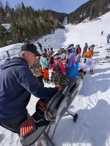 A person grills hot dogs on a snowy ski slope while others congregate nearby.