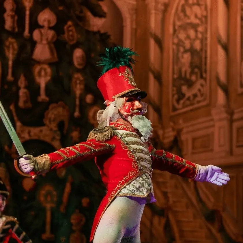 A performer dressed as the Nutcracker stands on stage with arms outstretched and a sword in one hand.