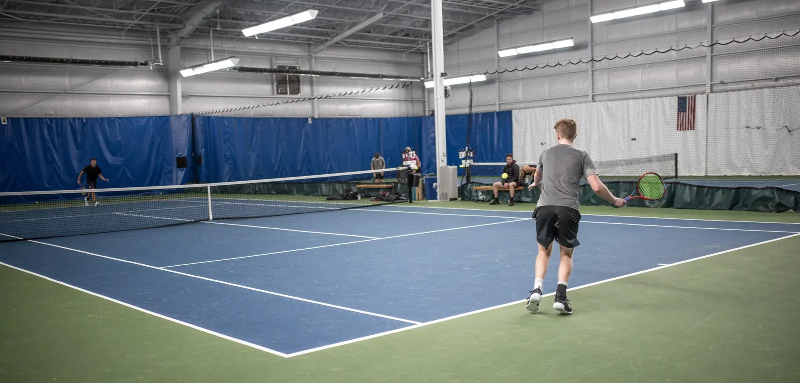 A young man plays tennis on an indoor court.