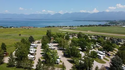 Photo from koa.com An aerial view of a recreational vehicle campground situated near a lake and mountains.