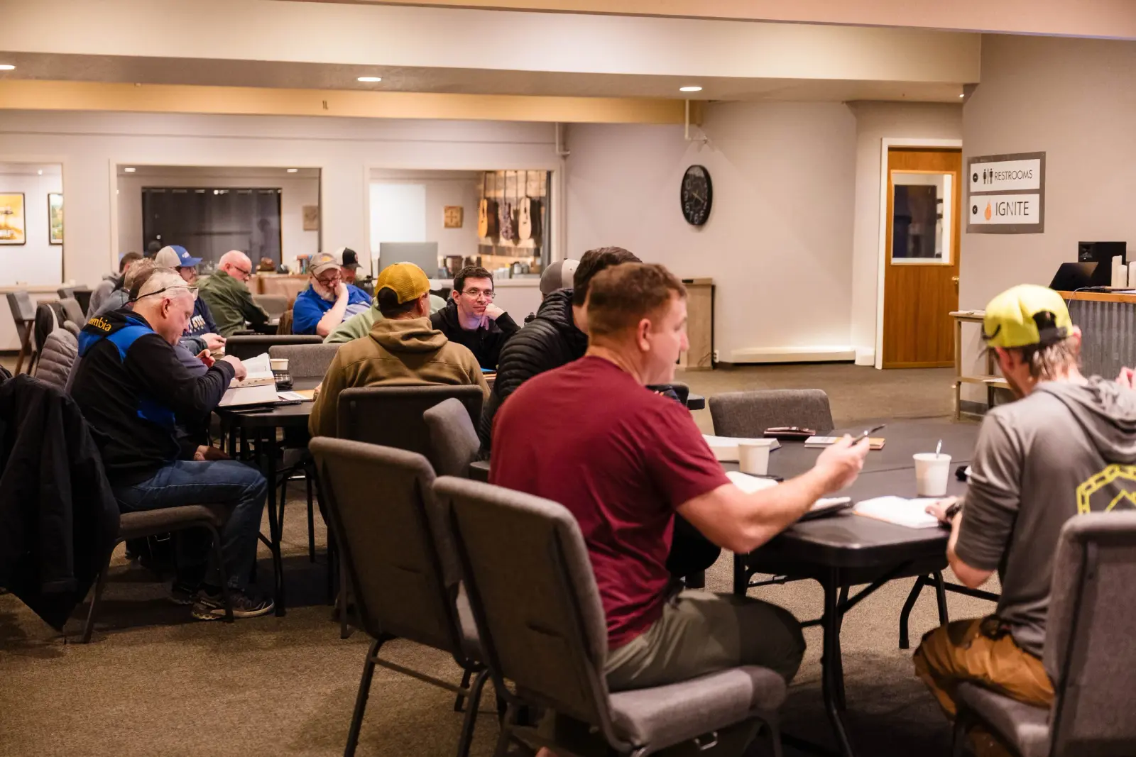 A group of men are sitting at tables in a room, seemingly engaged in a study or meeting.