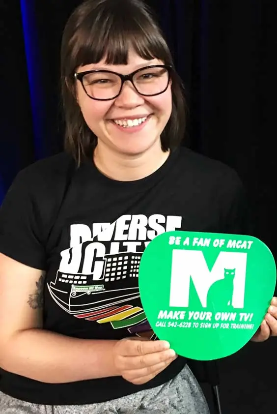A young woman holding up a green MCAT sign that says Be a Fan of MCAT - Make Your Own TV.