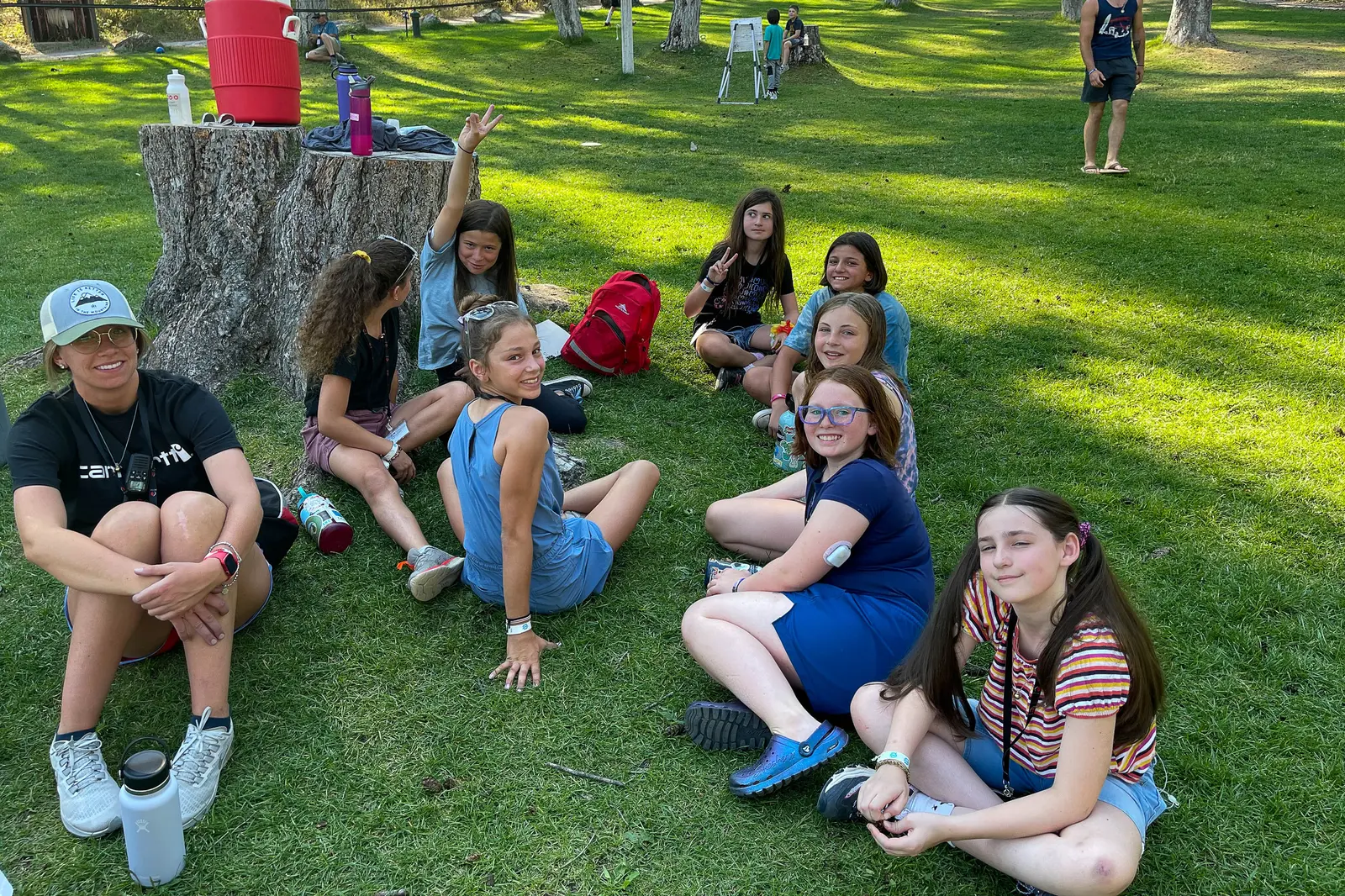 A group of young people and an adult sit on the grass outdoors.