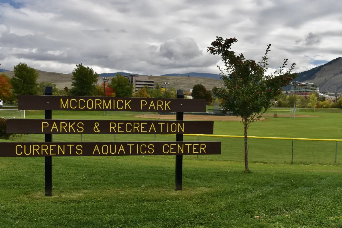 A wooden sign stands in a grassy park, identifying the location as McCormick Park and Currents Aquatics Center.