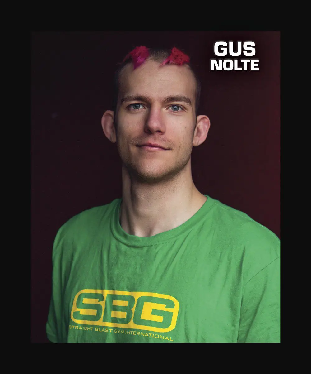 A portrait of a person with bright pink hair wearing a green t-shirt with a gym logo.