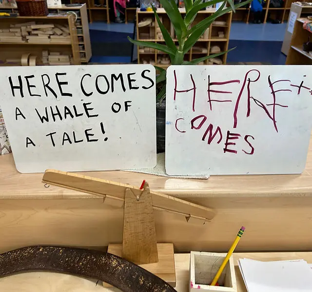 Two small whiteboards with handwritten text rest on a wooden surface in a classroom setting.