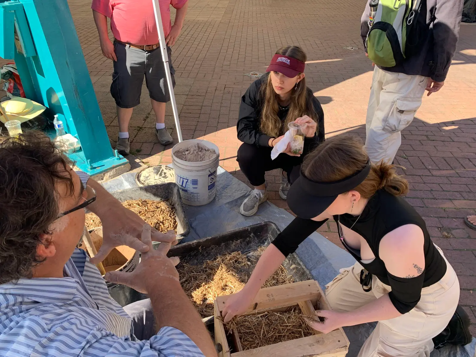 People participate in an interactive demonstration involving organic building materials on an outdoor plaza.