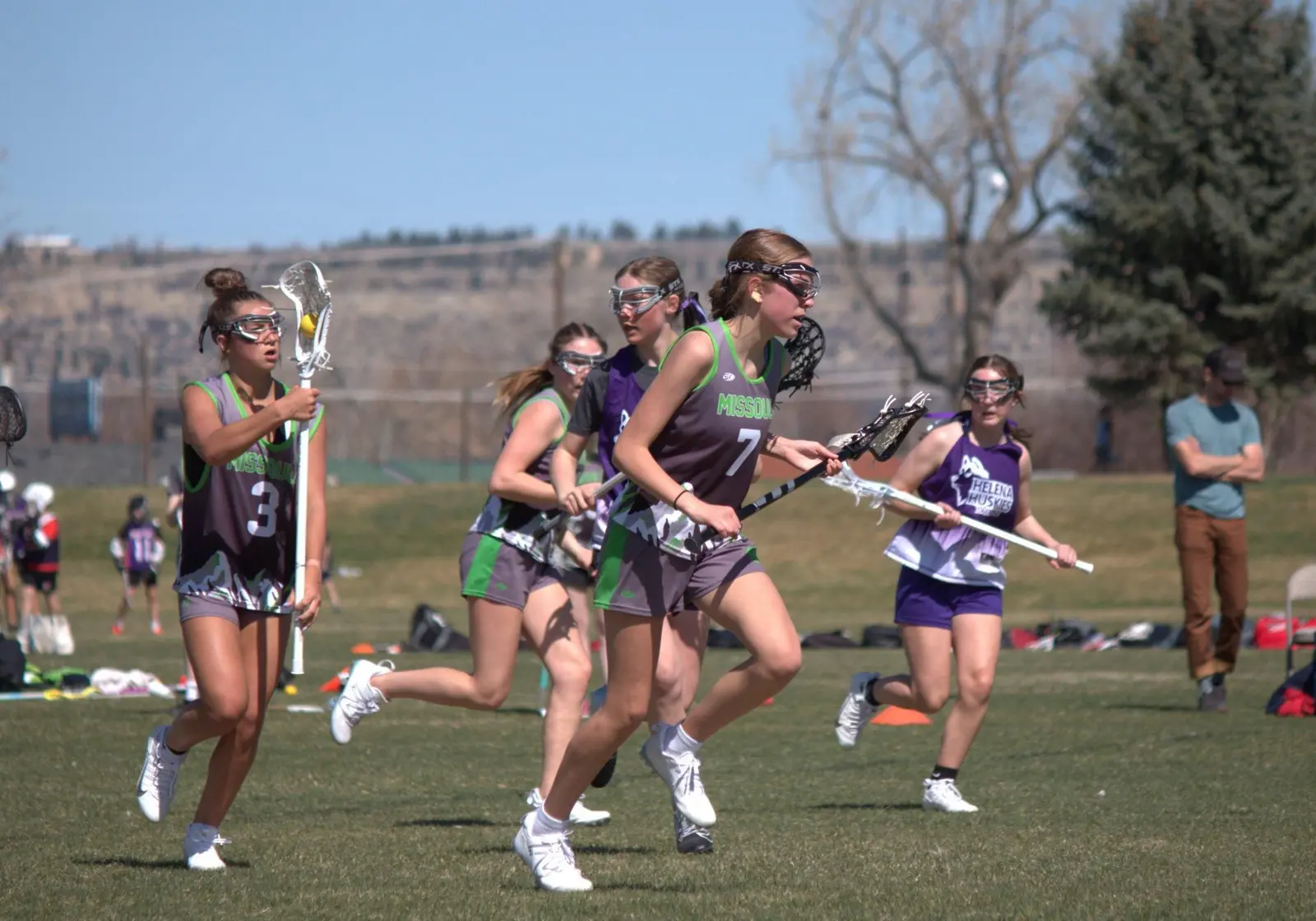 A group of female lacrosse players run across a field during a game.