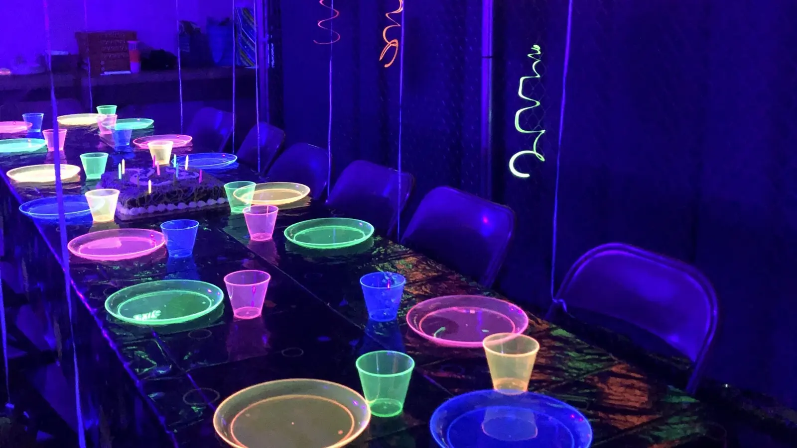 A table is set with neon-colored plates and cups in a room lit by blacklight.