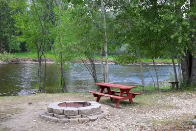 Photo from blackrabbitrv.com A picnic table is sitting next to a fire pit by a river.