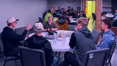 A group of young adults sit around a circular table in an indoor space.