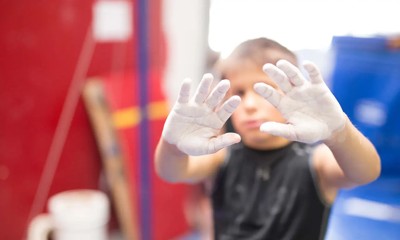 A child holds up hands covered in white gymnastics chalk.