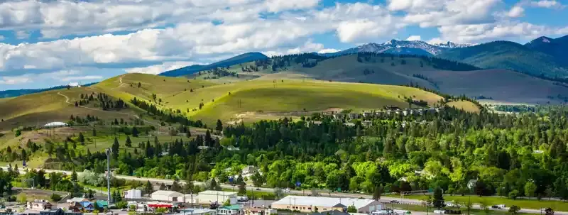 An elevated view of a landscape featuring rolling green hills, a forest, and a town area below.