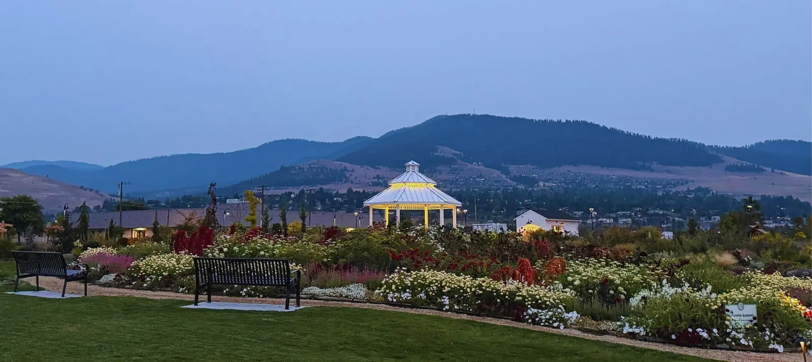 A garden with benches and a gazebo at dusk, backed by mountains.