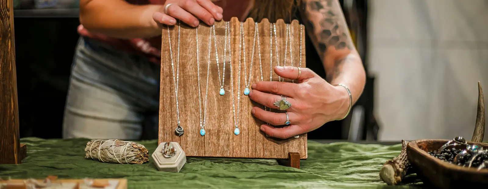 A person displays a collection of necklaces on a wooden stand.