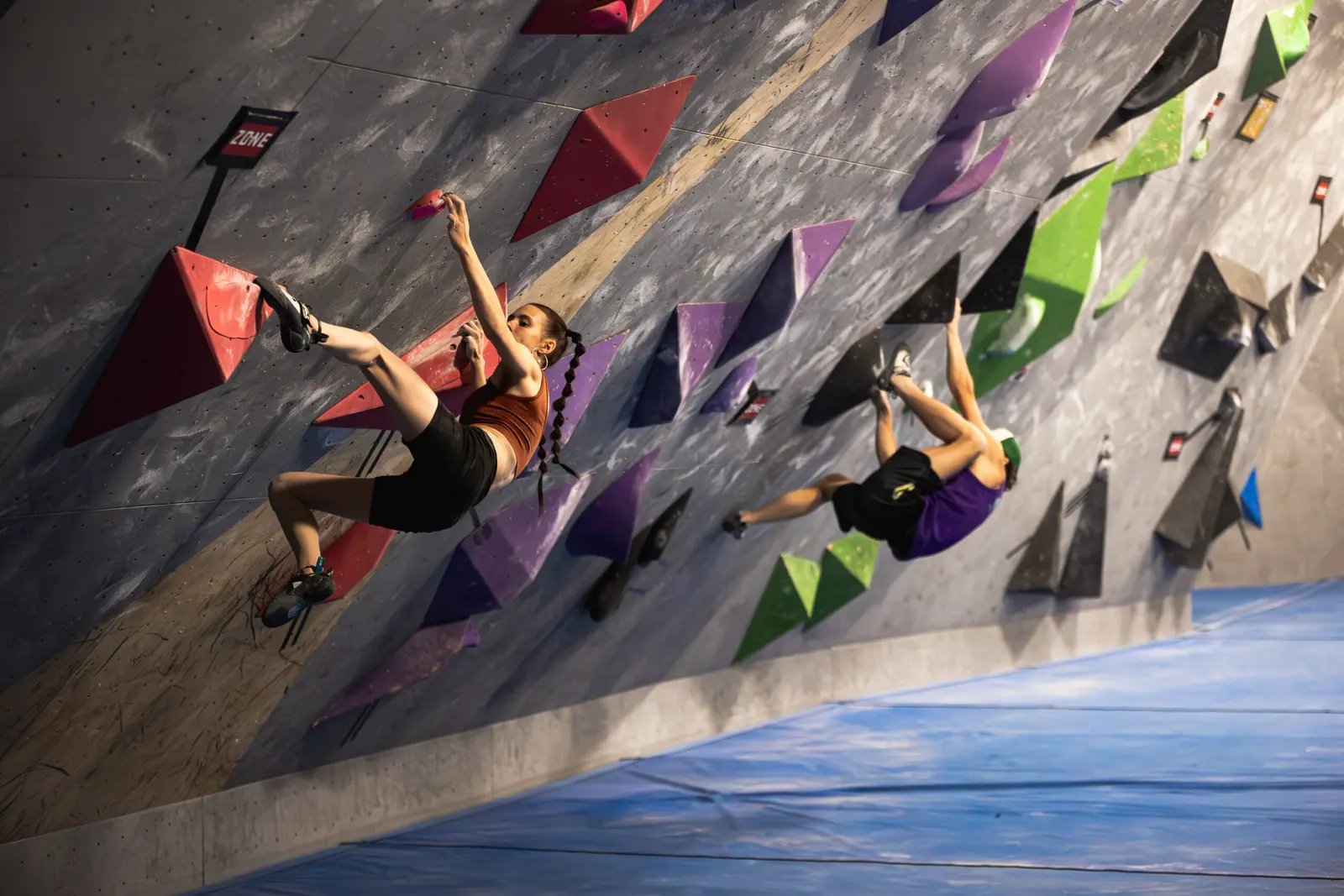 Two people are bouldering on an indoor climbing wall.