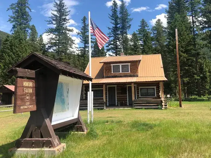 Monture Guard Station Rental Cabin in the Summertime. An American Flag Waves in the Front Yard. Monture Guard Station Rental Cabin in the Summertime.