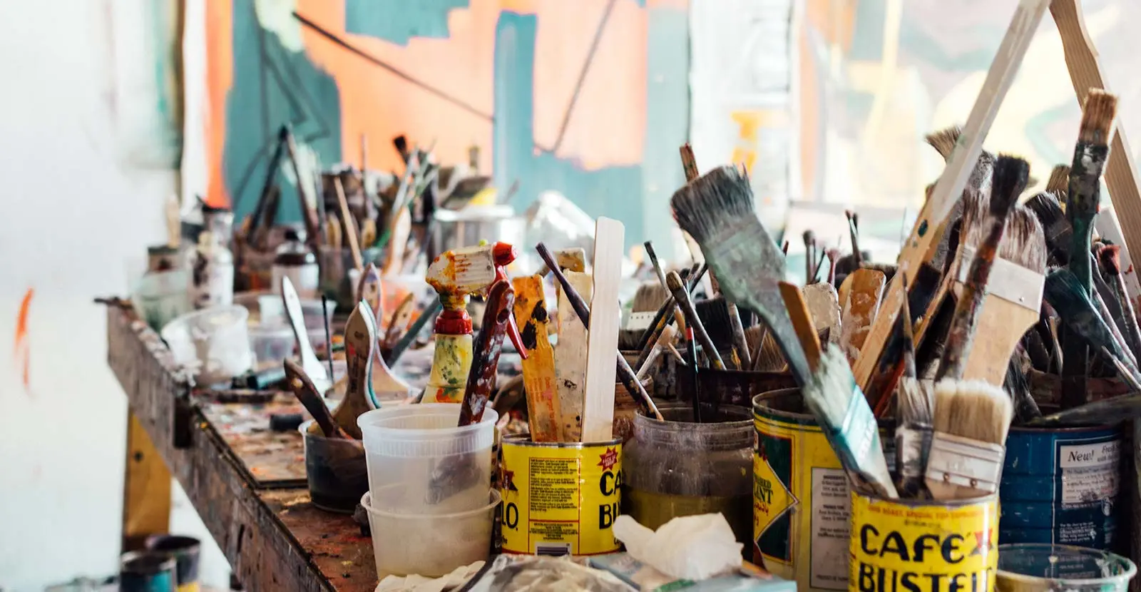 An array of paintbrushes and mixing tools sits in various containers on an artist's workbench.