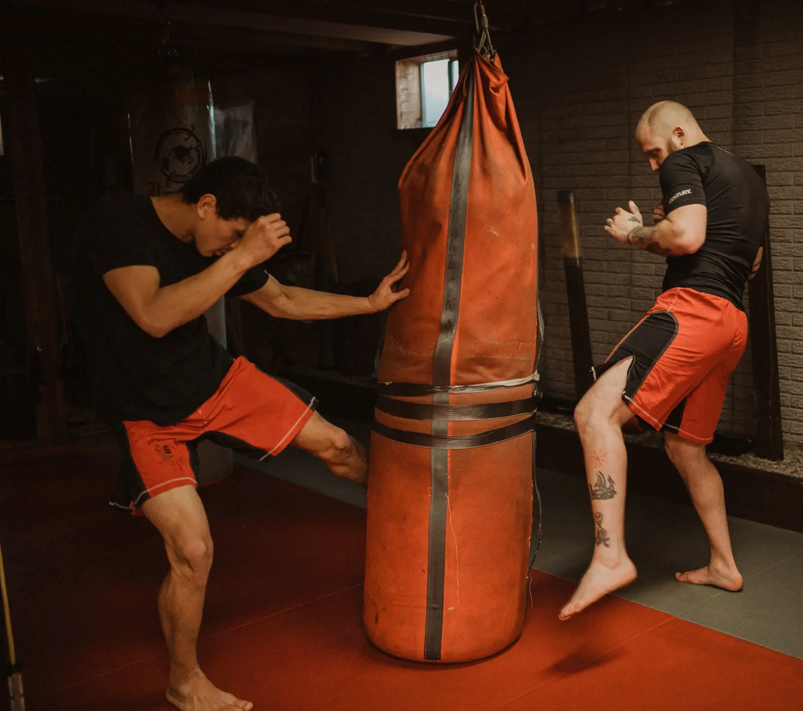 Two men are practicing kickboxing with a punching bag in a studio.