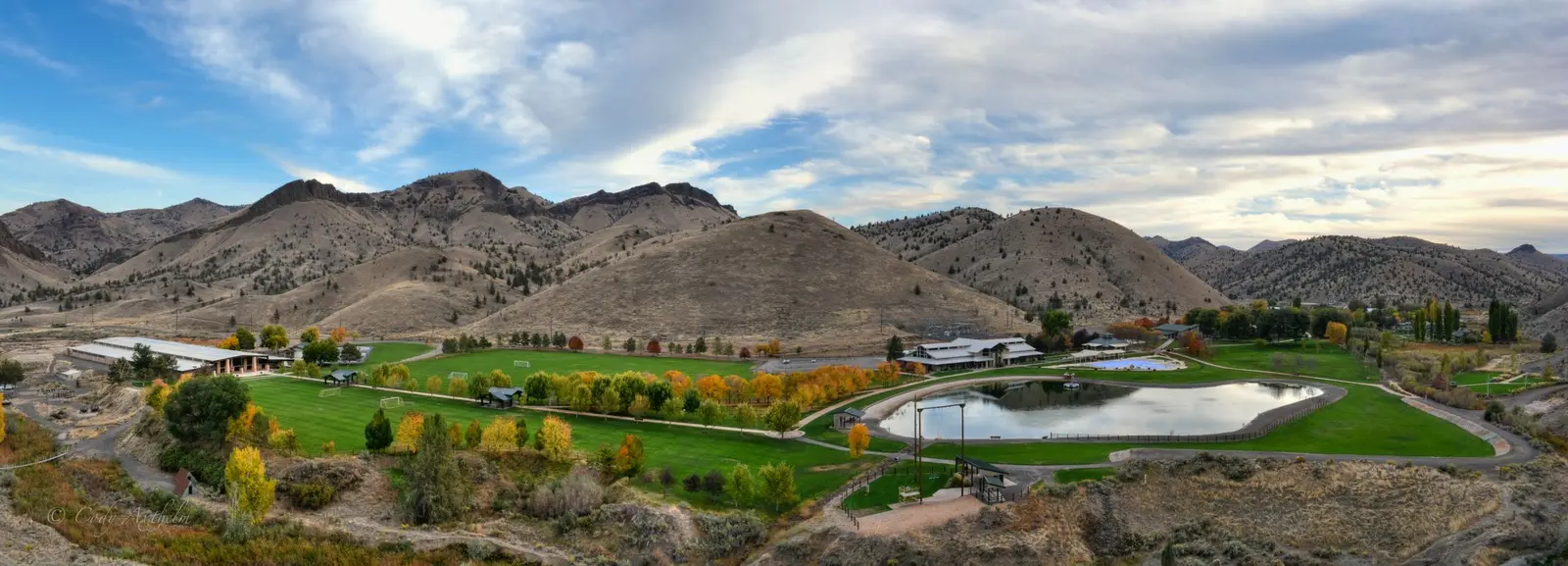 A wide-angle panoramic view shows a green landscape with buildings, a small lake, and hills in the background.