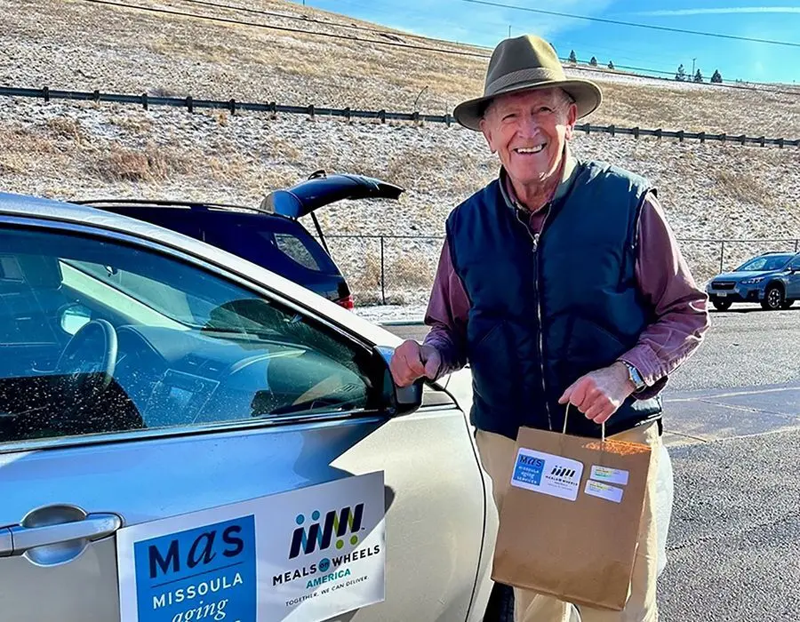 two older men smiling while holding bags to deliver meals for meals on wheels