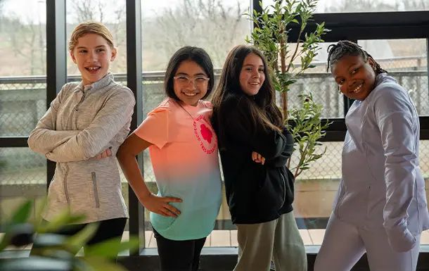 Four young people stand together smiling in a brightly lit indoor space.