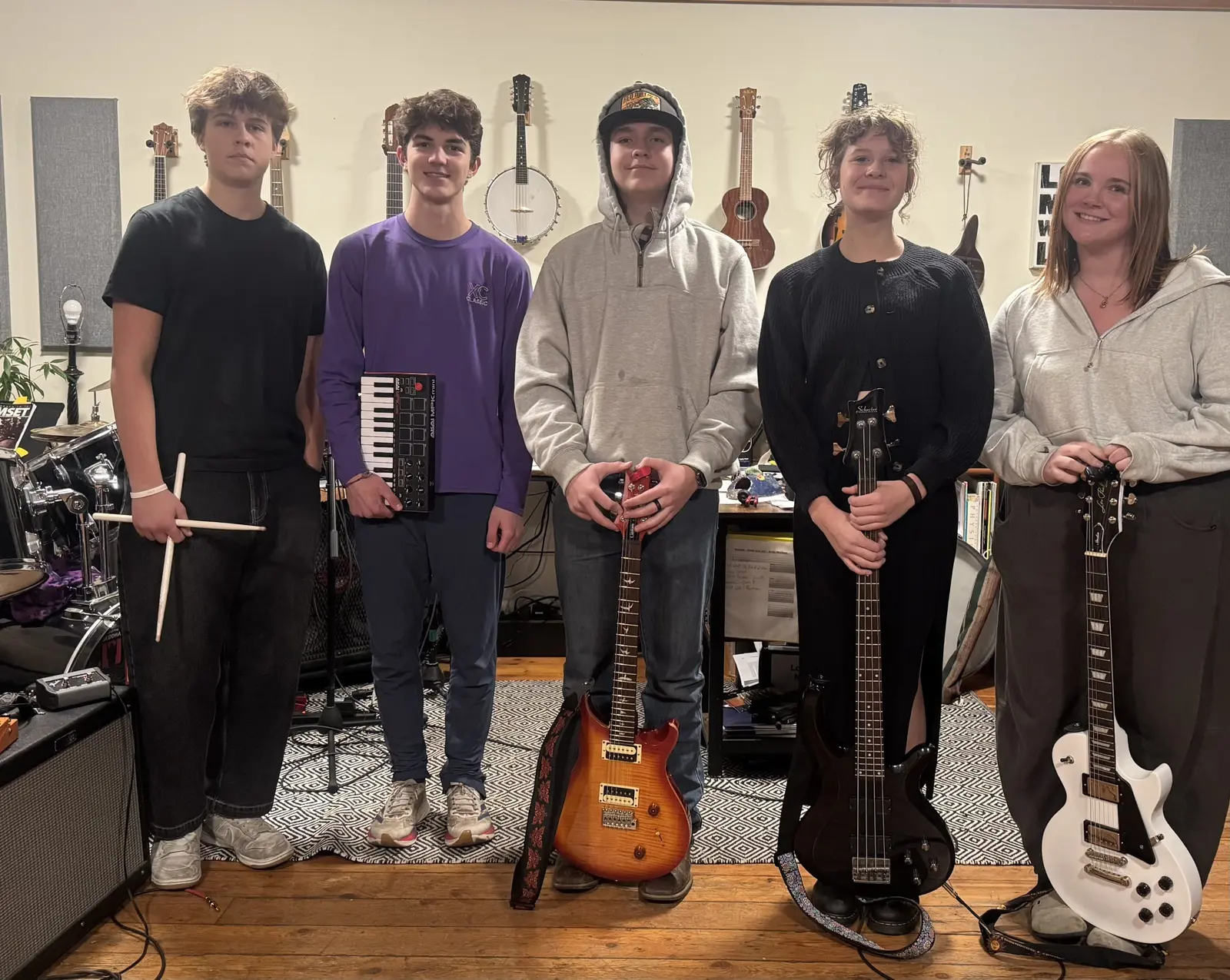 Five young people stand in a studio holding various musical instruments.
