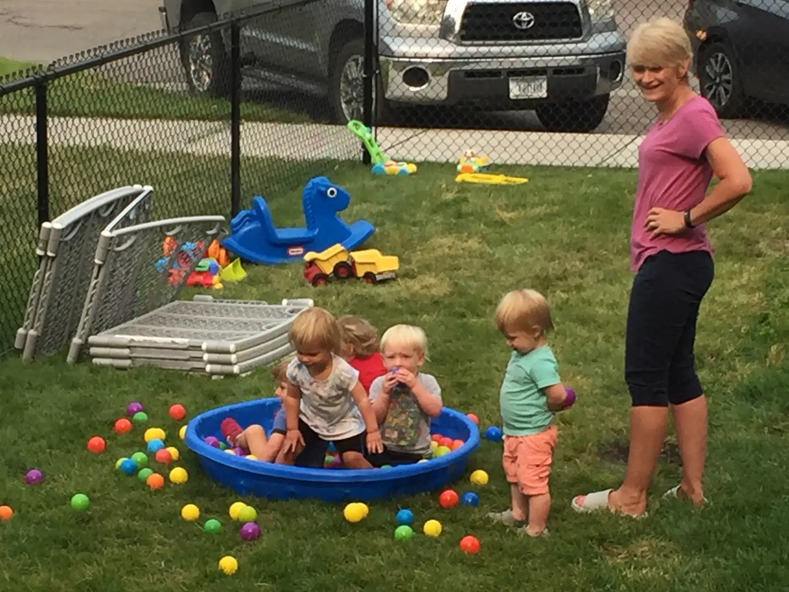 An instructor watches several young children playing in a ball pit outdoors.