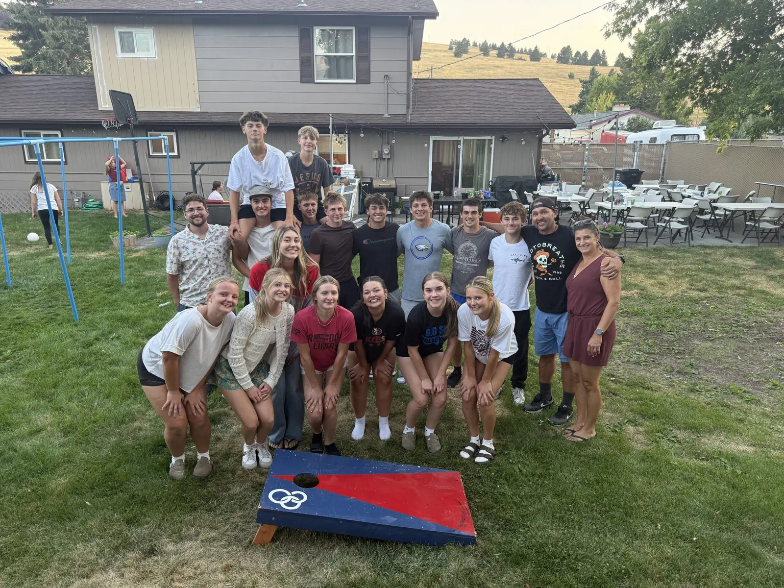 A large group of teenagers and young adults poses for a photo on a lawn in front of a house.