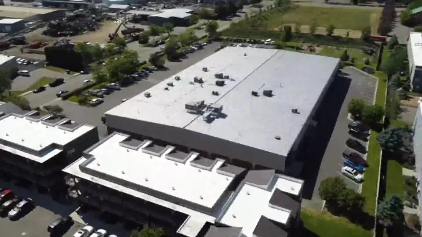 An aerial view shows commercial buildings surrounded by parking lots and landscaping.