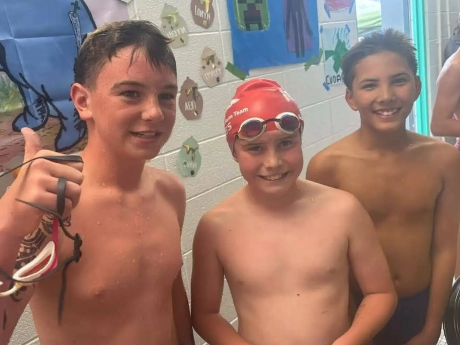 Three young swimmers stand together posing for a photo.