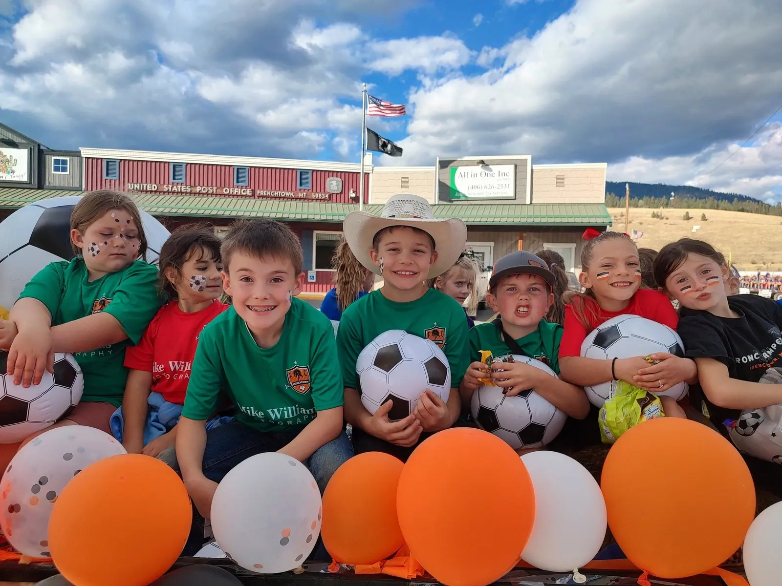 A group of children holding soccer balls and balloons pose for a photograph outside.