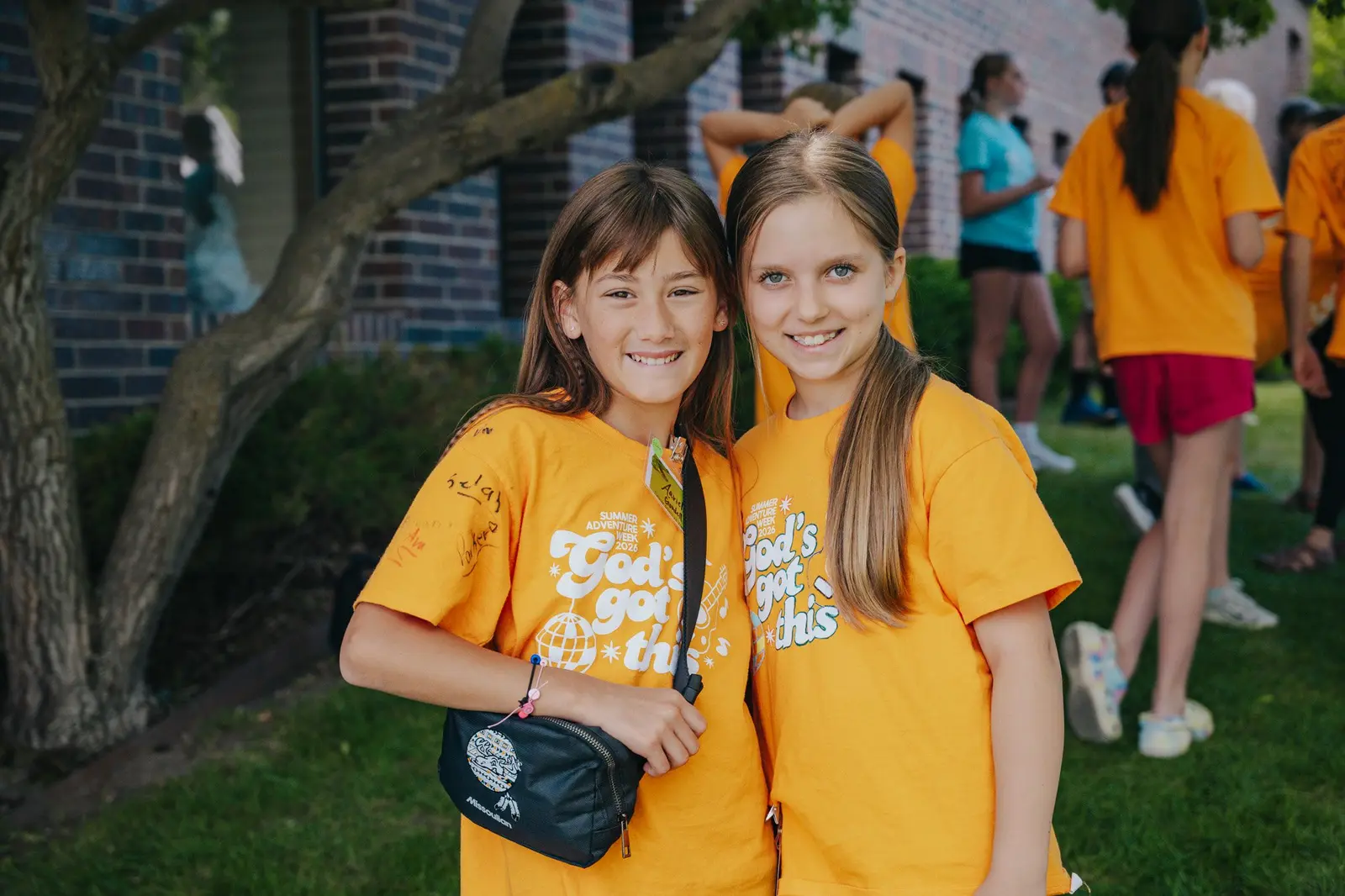 Two young girls wearing matching yellow shirts smile for the camera outdoors.