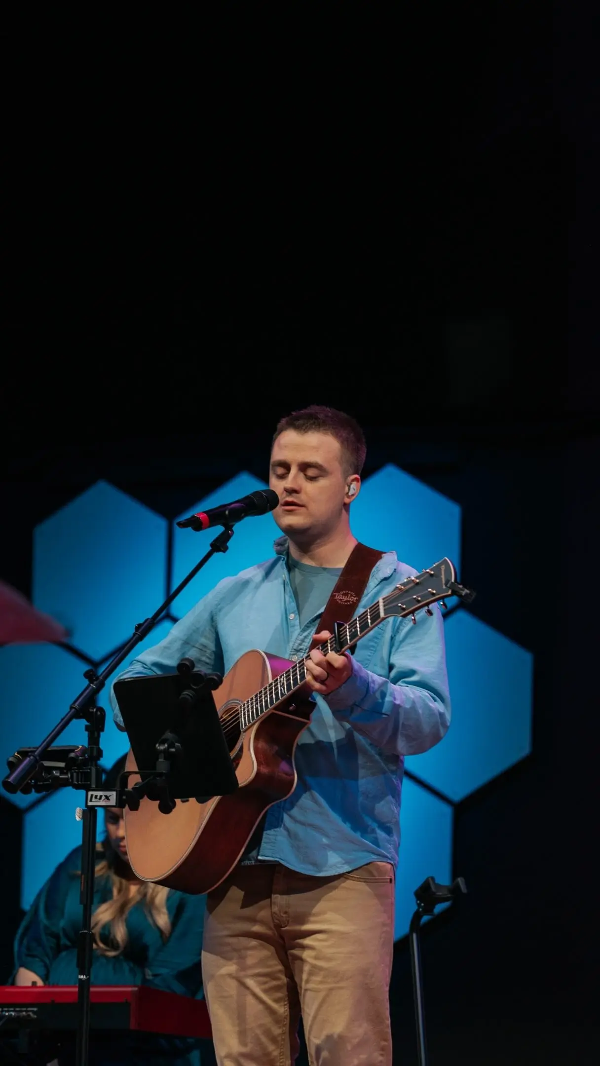 A man plays an acoustic guitar and sings into a microphone on stage.